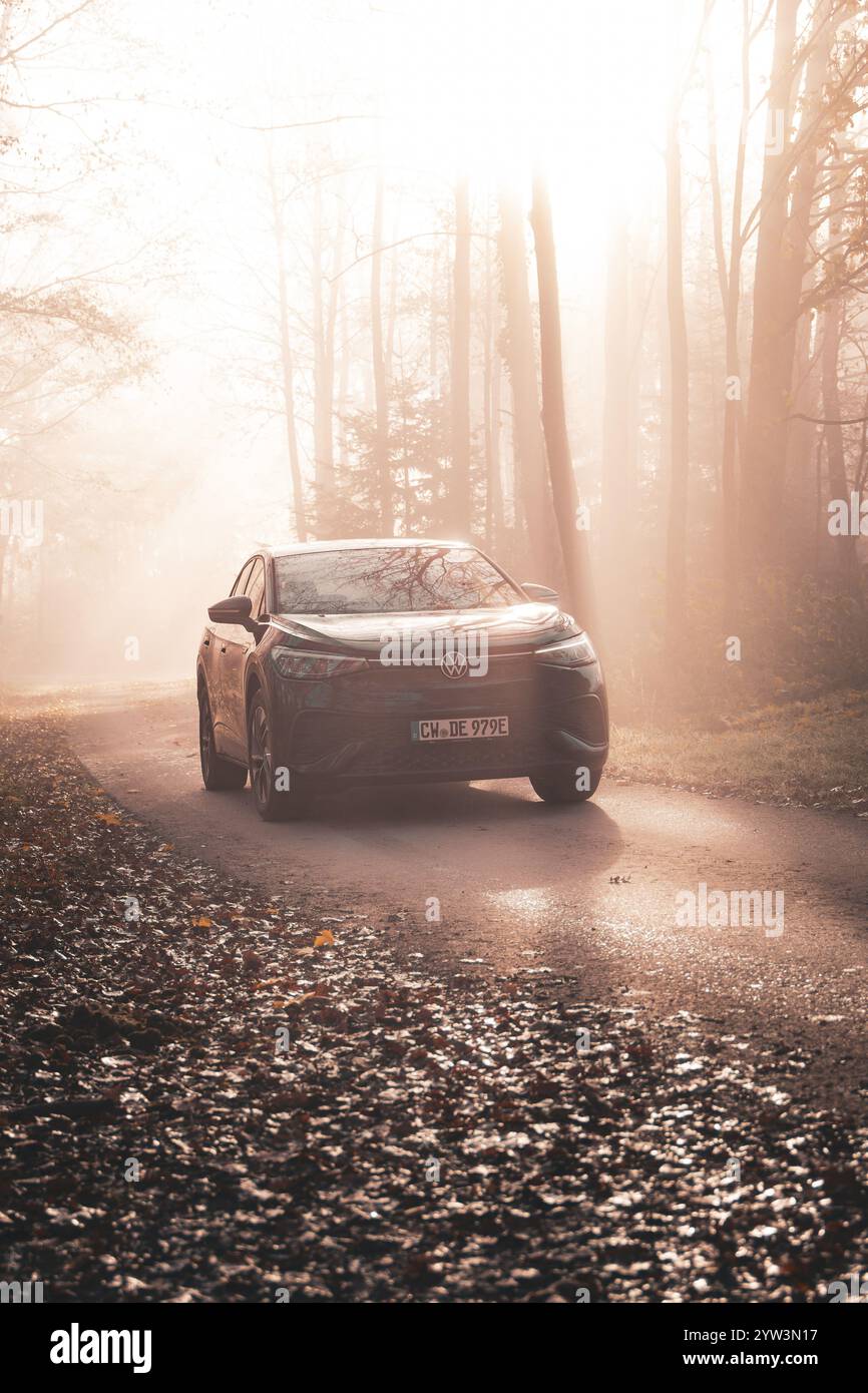 Bei Nebel und hellem Sonnenlicht steht ein Auto auf einer herbstlichen Forststraße, Elektroauto VW ID5, Deer Carsharing, Gechingen, Schwarzwald, Deutschland, Europa Stockfoto