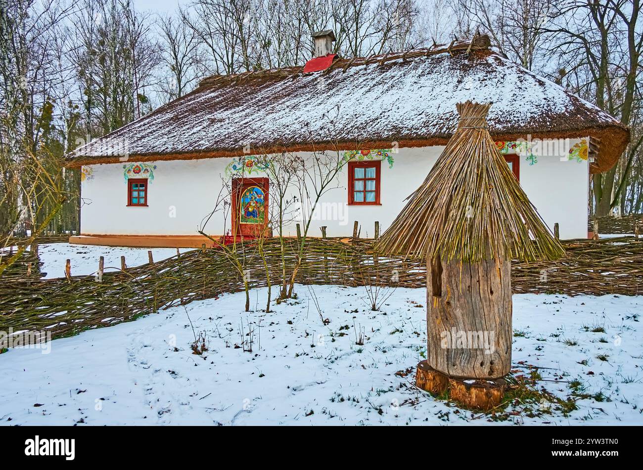 Das weiß getünchte hata-Haus des Imkers mit Blumenmustern, Strohdach, Korbzaun und dem Baumstamm im Vordergrund, Winter Pereiaslav SC Stockfoto