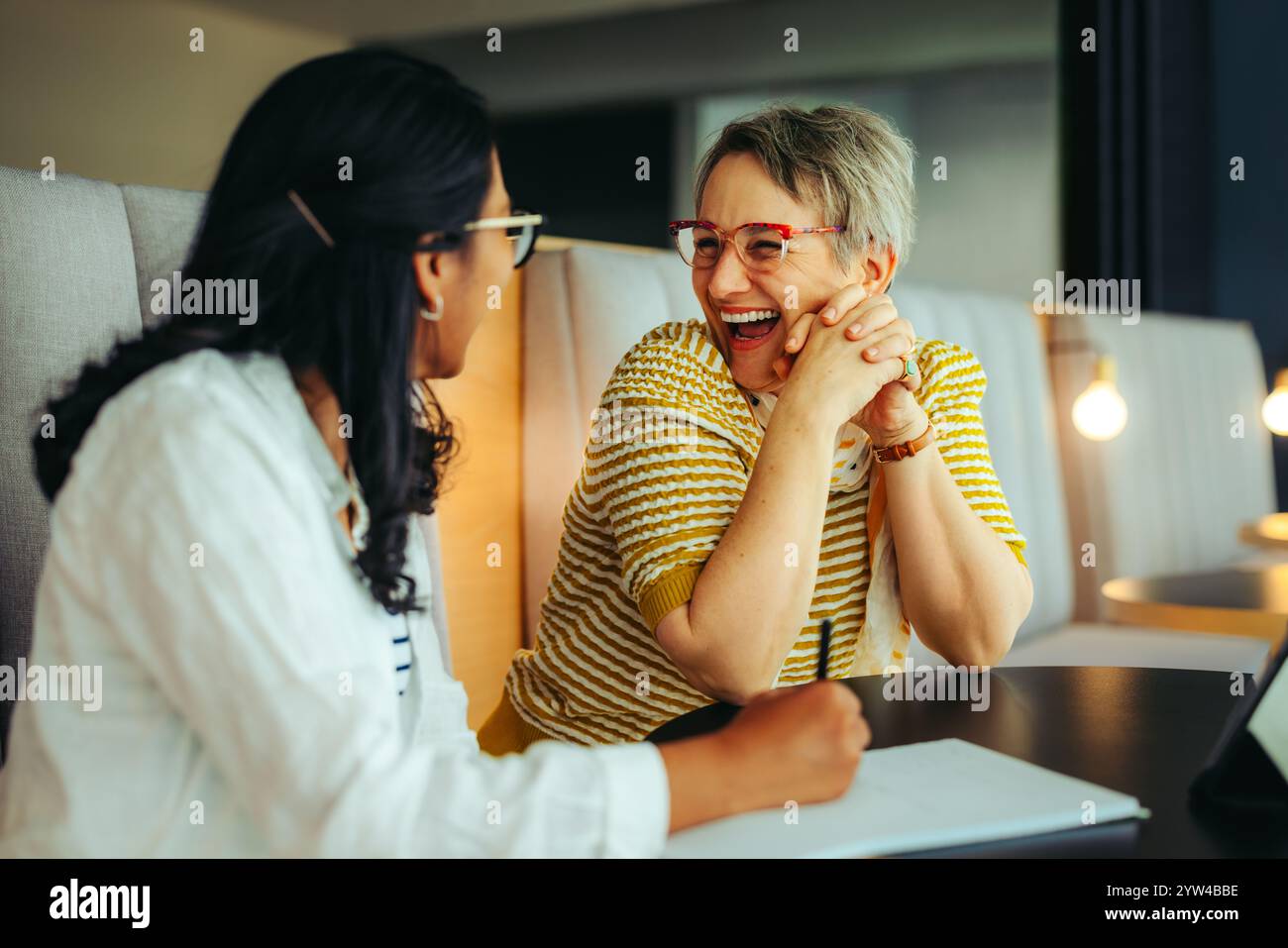 Eine stolze Lehrerin teilt einen Moment des Lachens mit einer Schülerin in einer Bibliothek und unterstreicht die Freude am Unterrichten und gemeinsamen Lernen in einem insp Stockfoto