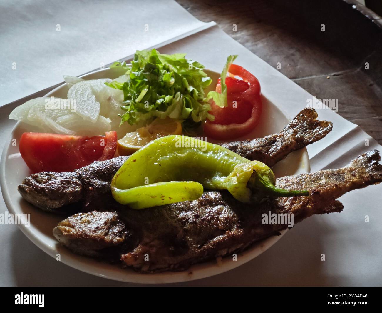 Ein Teller traditioneller türkischer Izgara Balık oder gegrillter Fisch, serviert mit grünem türkischem Chili (sivri biber), Tomaten in Scheiben, Zwiebeln und Salat Stockfoto