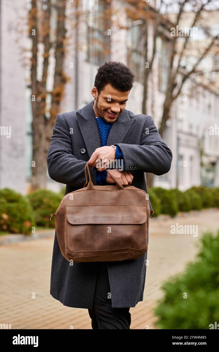 Ein stilvoller Mann sieht fröhlich aus, während er seine braune Tasche an einem angenehmen Tag im Freien inspiziert Stockfoto