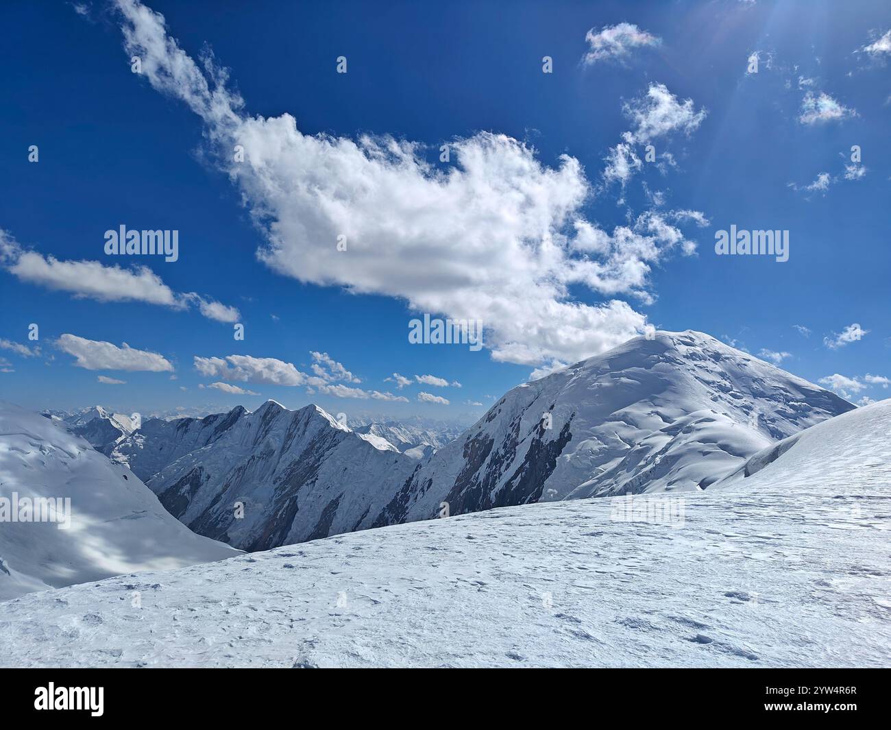 Die ruhige Berglandschaft bietet schneebedeckte Gipfel unter einem leuchtend blauen Himmel mit weichen Wolken. Stockfoto