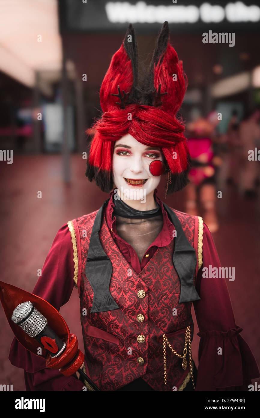 Ein Nahporträt einer hübschen Cosplayerin, die als Alastor aus dem Hazbin Hotel verkleidet ist, lächelnd und lustig auf einer UK Comic Con-Veranstaltung Stockfoto