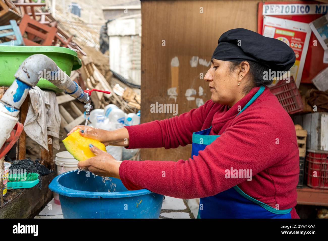 Lurin, Lima, Peru – 6. September 2024: Eine peruanische Frau in Rot gekleidet mit einem schwarzen Küchenhut wäscht Kürbisstücke in einem Eimer im kommunalen Ki Stockfoto