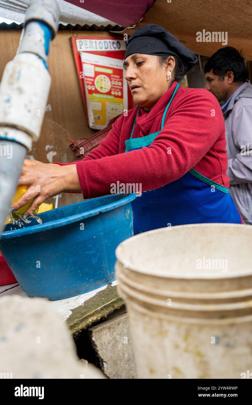 Lurin, Lima, Peru – 6. September 2024: Eine peruanische Frau in Rot gekleidet mit einem schwarzen Küchenhut wäscht Kürbisstücke in einem Eimer im kommunalen Ki Stockfoto