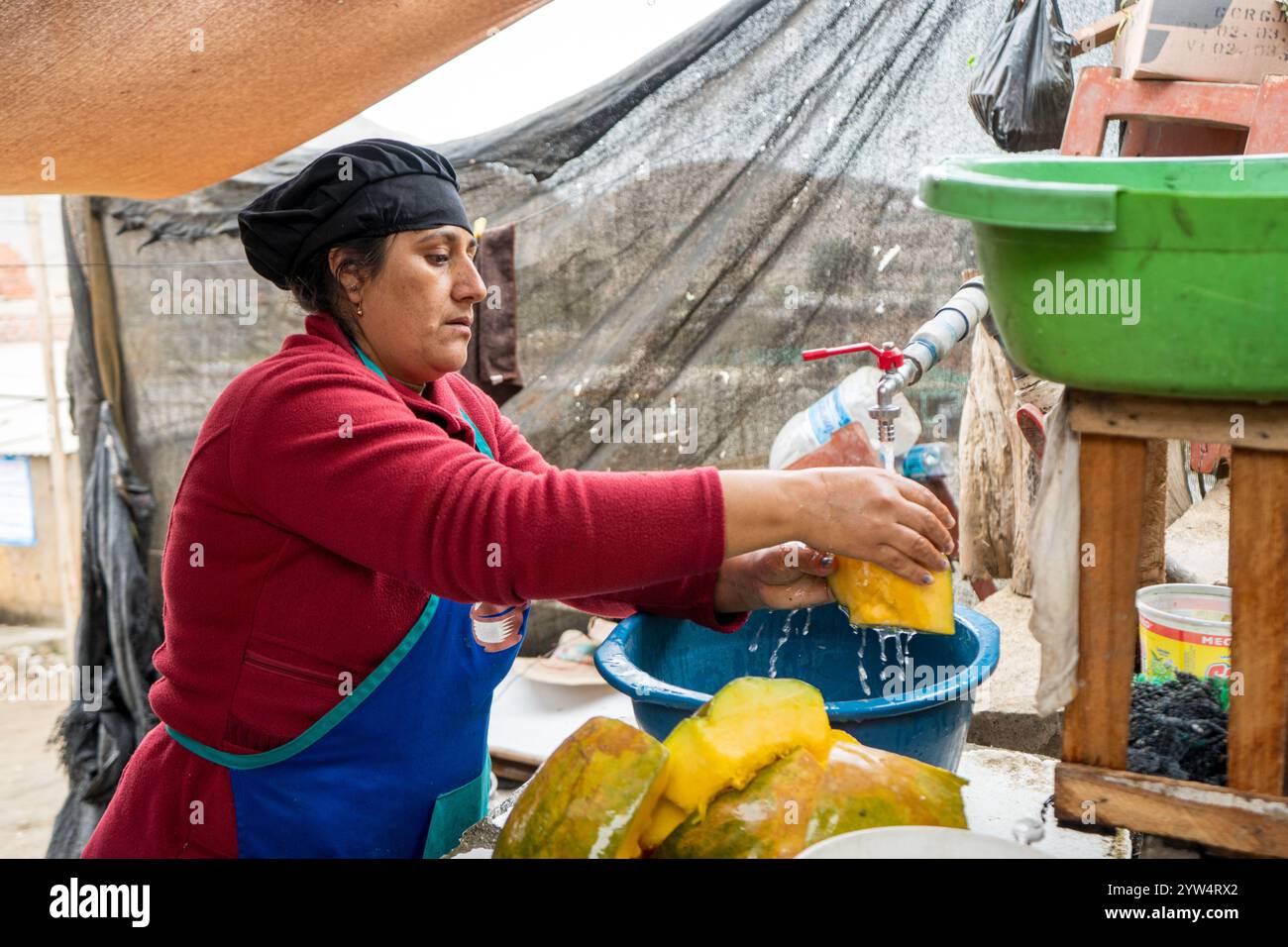 Lurin, Lima, Peru – 6. September 2024: Eine peruanische Frau in Rot gekleidet mit einem schwarzen Küchenhut wäscht Kürbisstücke in einem Eimer im kommunalen Ki Stockfoto