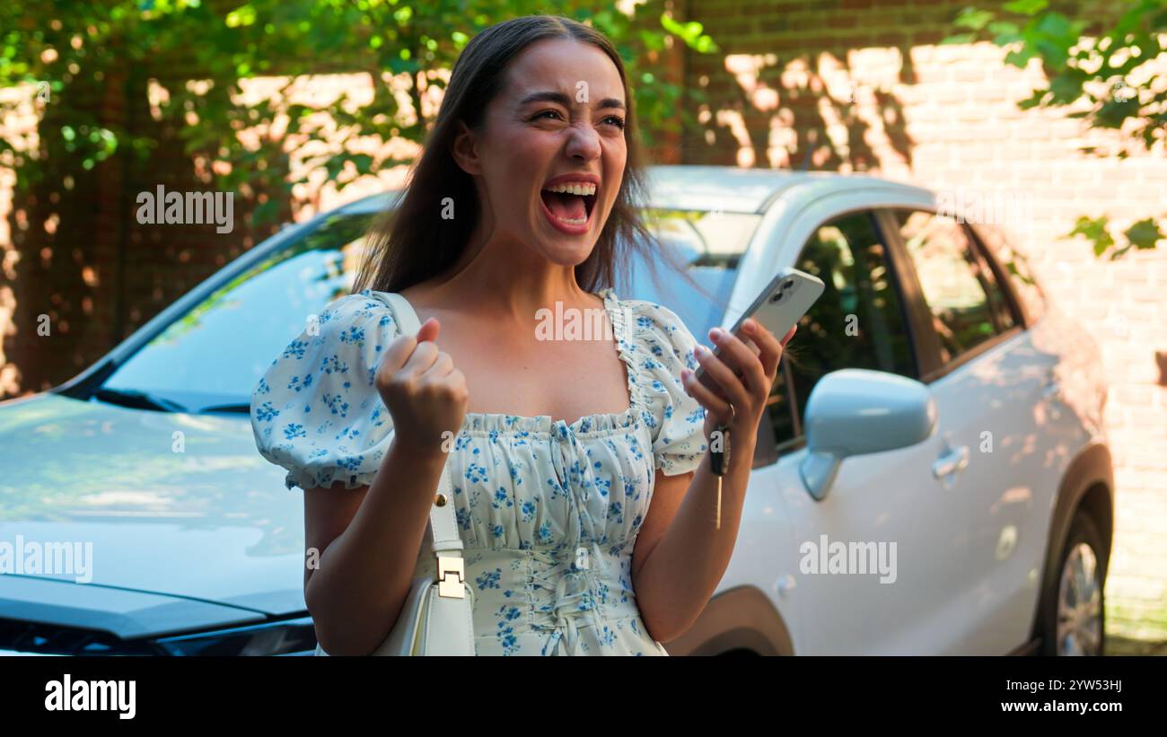Überrascht überrascht Kaukasiens positiver Schock Frau weibliche Automobilfahrerin Autokäufer Glückliches Mädchen mit Handy hält Smartphone aufgeregt Stockfoto