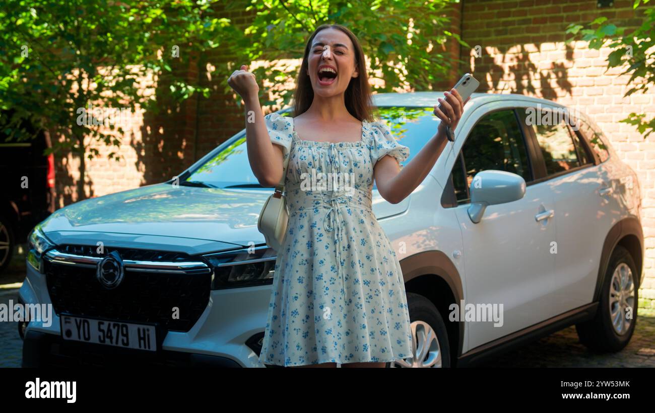 Aufgeregt schockiert Kaukasierin weibliche Käuferin Klientelfahrerin Gewinnerin mit Handy lesen große Nachrichten schreien Erfolg gewinnen Gestenwette gewinnen Auto gewinnen Stockfoto