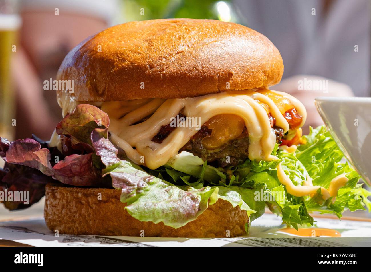 Köstlicher Burger aus der Nähe, zubereitet mit einem saftigen Patty, garniert mit geschmolzenem Käse, frischem Salat und großzügiger Soße, die eine perfekte Balance zwischen den Gerichten schaffen Stockfoto