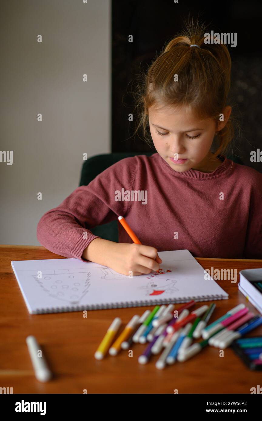 Das Mädchen sitzt auf dem Tisch, sie studiert Malen und Lesen mit vielen Markierungen und Bleistiften Stockfoto