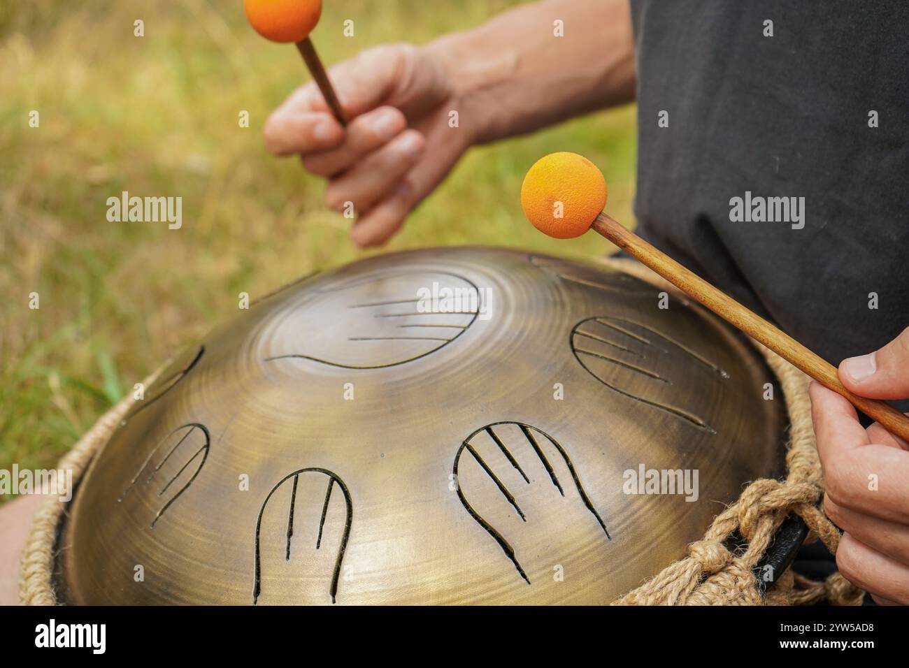Ein junger Mann spielt die Handpfanne. Eine Szene mitten im Wald. Der klangliche Klang eines Xylophons wird mit der Melodie des Raumes assoziiert Stockfoto