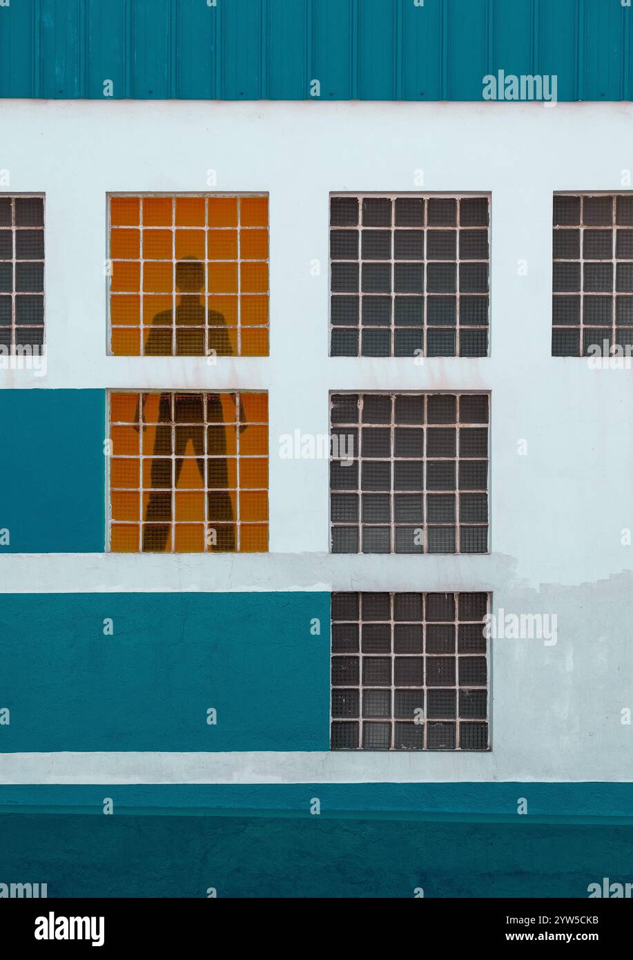 Mann, der hinter einem Fenster in einem Industriegebäude steht. Stockfoto