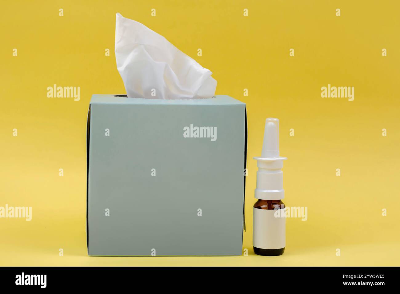Auf dem Bild befindet sich eine Schachtel mit Gewebe und ein Nasenspray auf gelbem Hintergrund. Die Dinge, die du brauchst, falls du eine Erkältung hast. Stockfoto