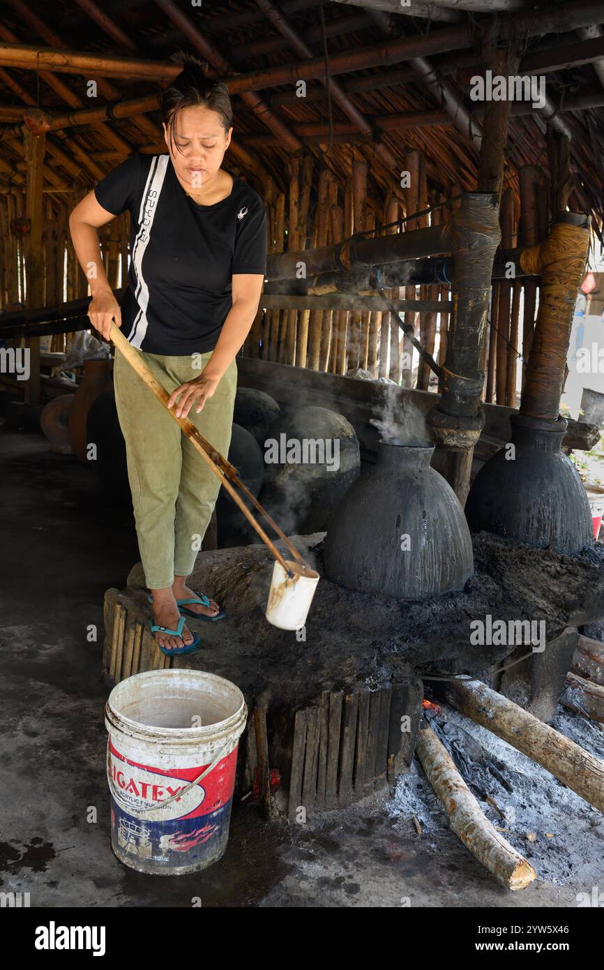 Aimere, Flores, Indonesien - Oktober 31 2024: Frau destilliert Arak-Liquor in einer traditionellen indonesischen Destillerie. Stockfoto