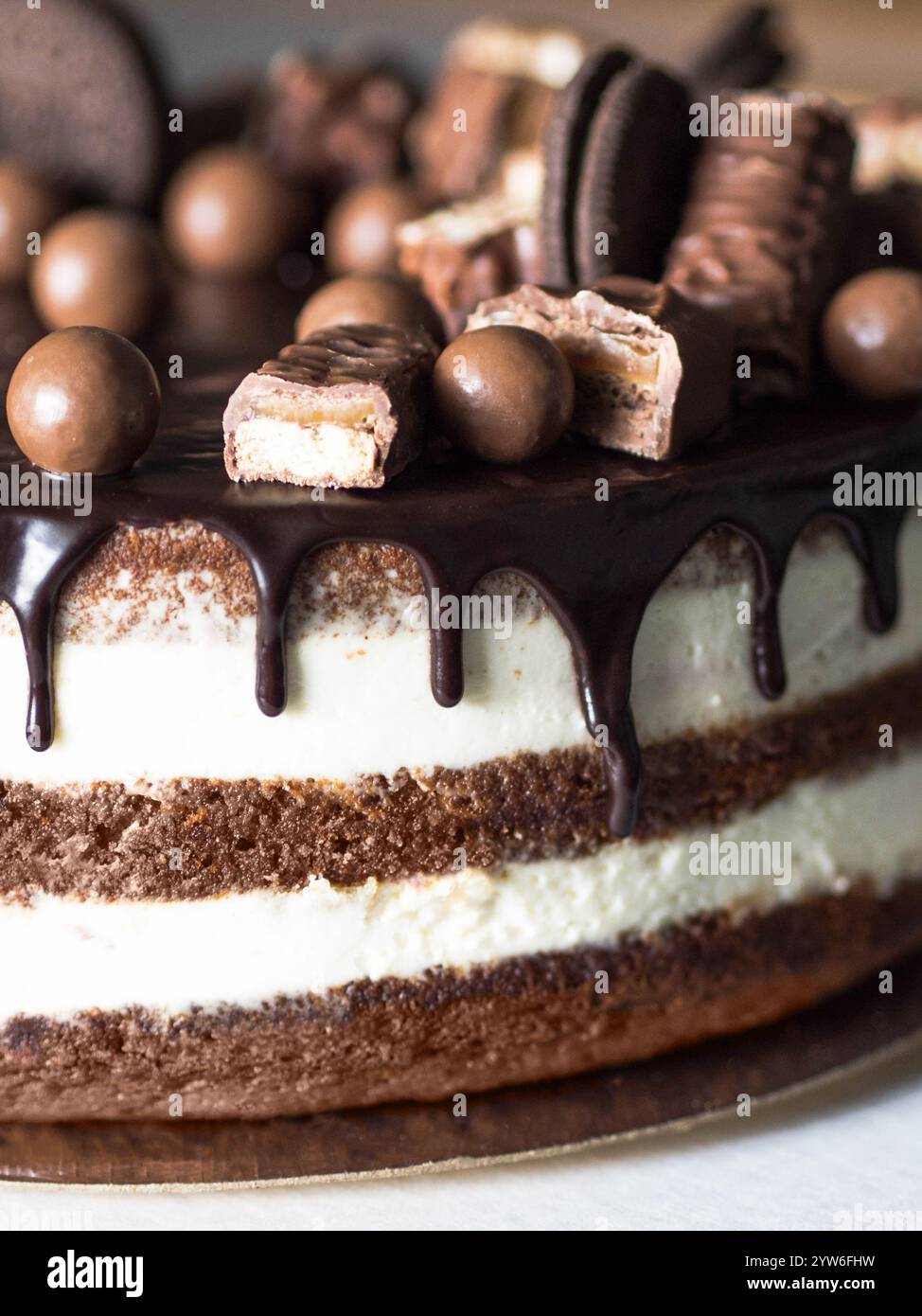 Nahaufnahme eines Schokoladenkuchens mit cremigen Schichten, bedeckt mit tropfender Schokoladenzuckerung, Schokoladenbonbons und -Bars. Zeigt die Farbe von 2025 yea Stockfoto