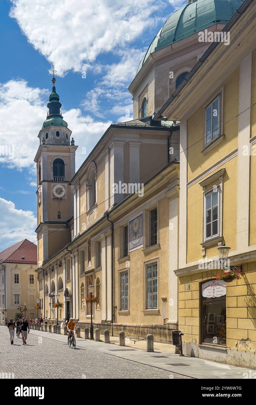 Ljubljana, Slowenien - 28. Juni 2024: Südfassade der Nikolaikirche mit Uhrenturm von der Einkaufsstraße Ciril-Metodov unter blauem cl Stockfoto