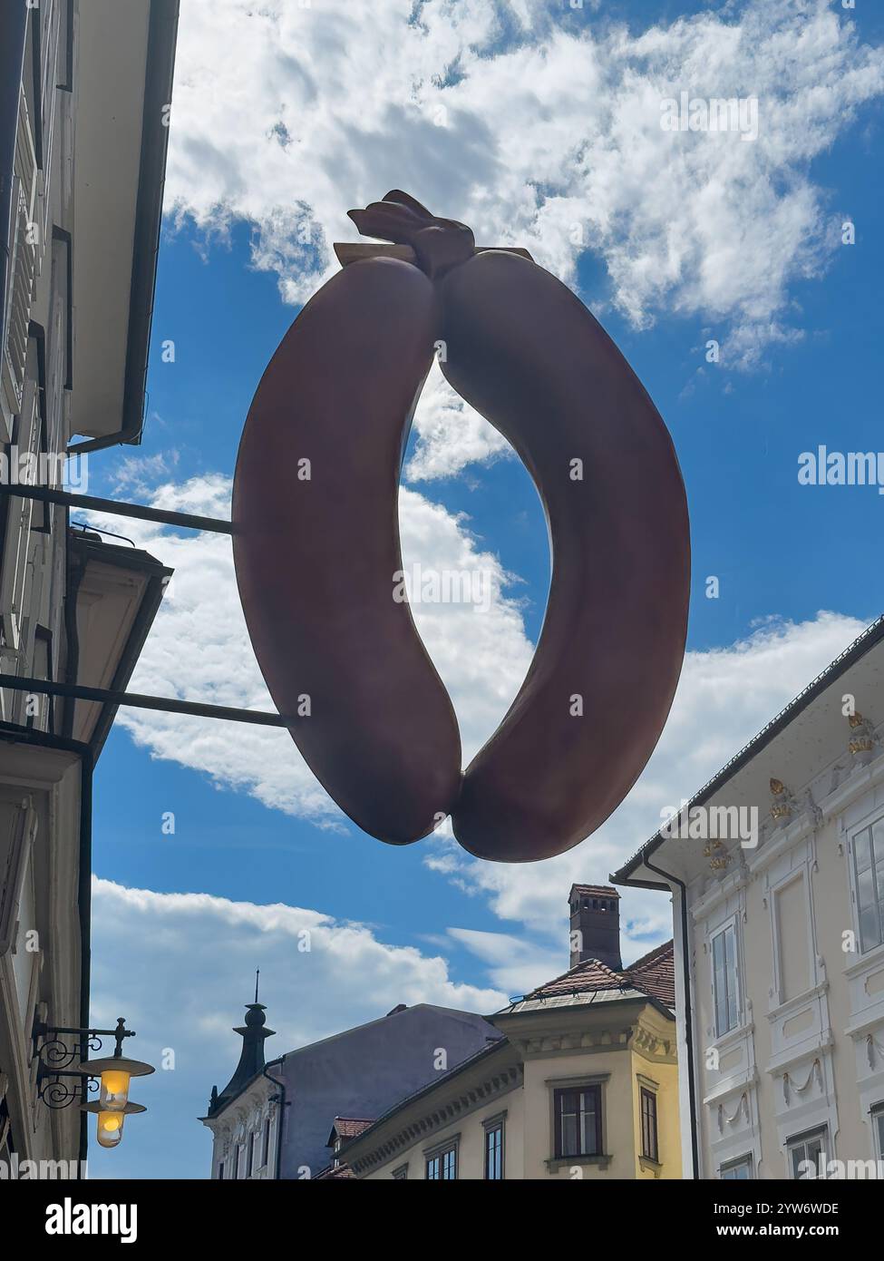 Ljubljana, Slowenien - 28. Juni 2024: Klobasarna-Wurstladen-Emblem, dreidimensionales Kunstwerk von 2 Blutwürsten vor blauer Wolkenlandschaft in Ciril-Metodo Stockfoto