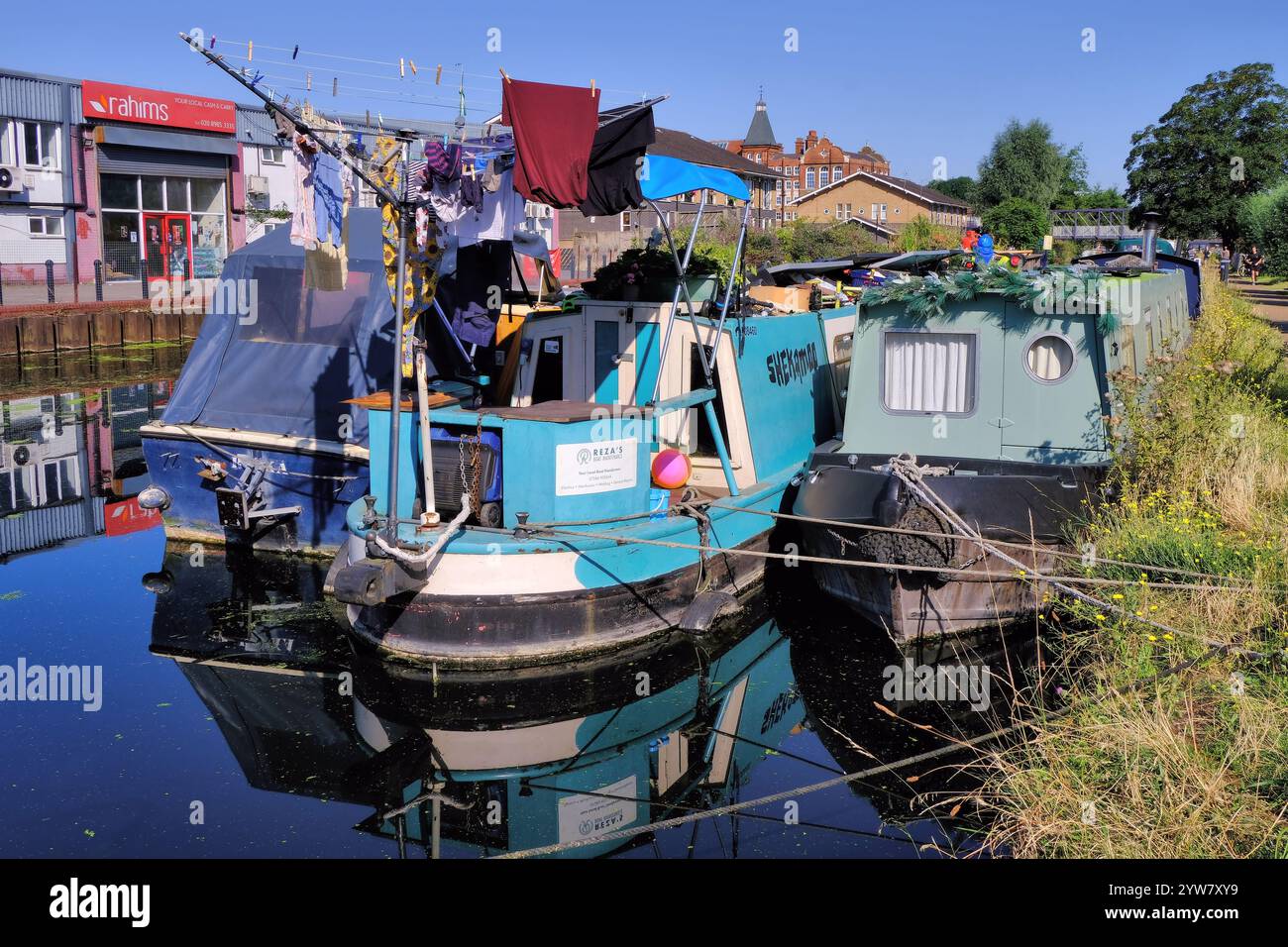 Farbenfrohe Kanalboote, Lastkähne, mit rotierender Wäscheleine und Spiegelreflexen auf River Lee Navigation in Stratford, London, England, Großbritannien Stockfoto