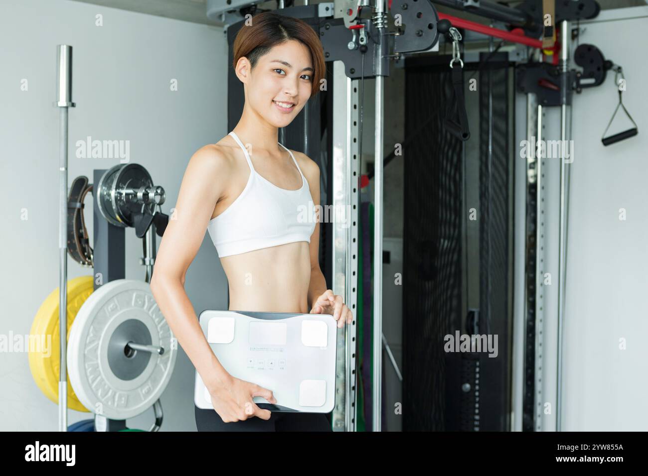 Eine junge Frau, die im Fitnessstudio eine Waage hält Stockfoto