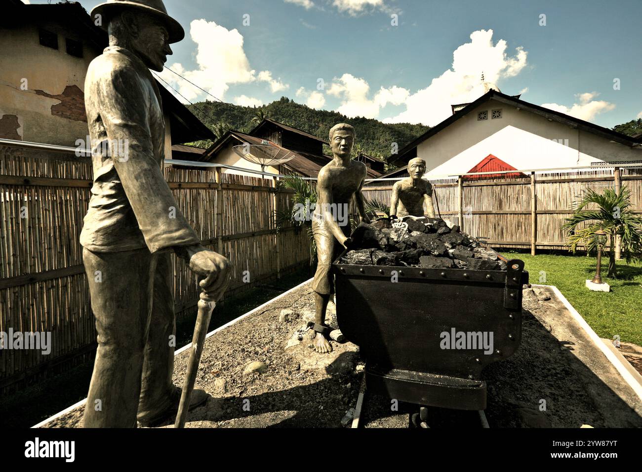 Skulpturen, die einen Aufseher zeigen, der Arbeiter beim Transport von Kohle mit einem Eisenbahnwagen in Sawahlunto, einer ehemaligen Kohlebergbaustadt in Sumatra, aufmerksam macht. Stockfoto