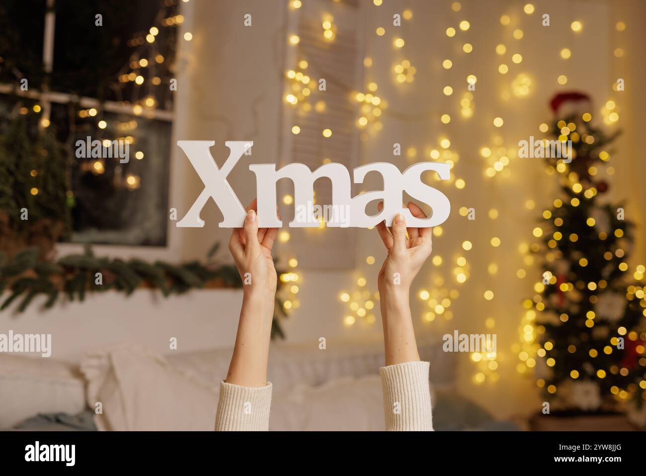 Frau, die WEIHNACHTSSCHILD mit weihnachtsbeleuchtung in ihrem Haus hält, gemütliche weihnachten Stockfoto