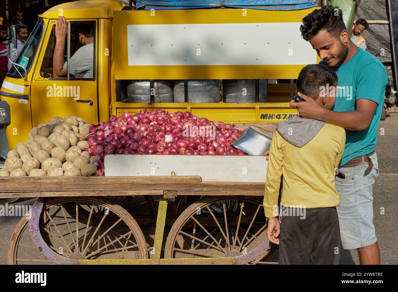 Ein Verkäufer, der Kartoffeln und Zwiebeln aus seinem Wagen verkauft, hält an, um seinen kleinen Bruder zu begrüßen und zu umarmen; in Dharavi Slum Area, Mumbai, Indien Stockfoto