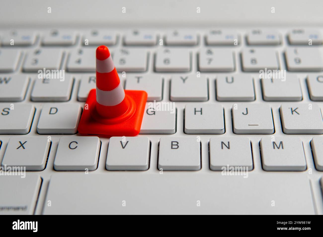 Ein Miniatur-Verkehrskegel auf einer Computertastatur. Website-Pflege, technische Schwierigkeiten, Website im Bau Konzept. Stockfoto