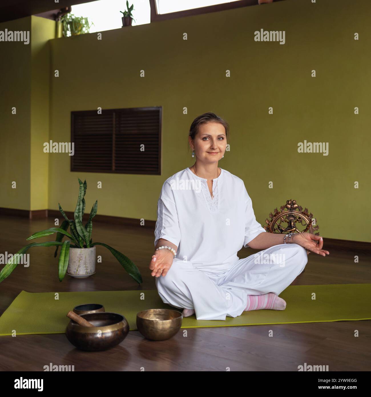 Frau übt Kundalini Yoga, Meditation, sitzt in Lotusposition auf einer Matte in einem Raum in weißer Kleidung, macht Jnana Mudra mit ihren Händen, eine Gestu Stockfoto