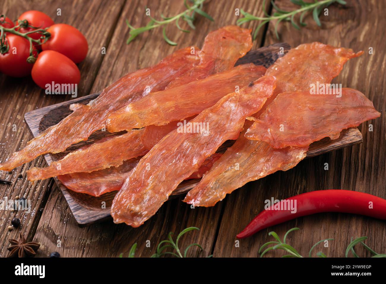 Geräucherte Hähnchenchips auf einem Holztisch mit Tomaten, Paprika und Rosmarin, Nahaufnahme-Snack für Bier Stockfoto
