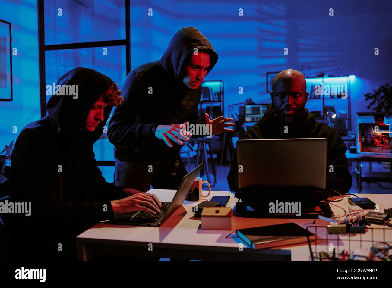 Birassische Hacker in schwarzen Hoodies diskutieren Programmdetails im Büro Stockfoto