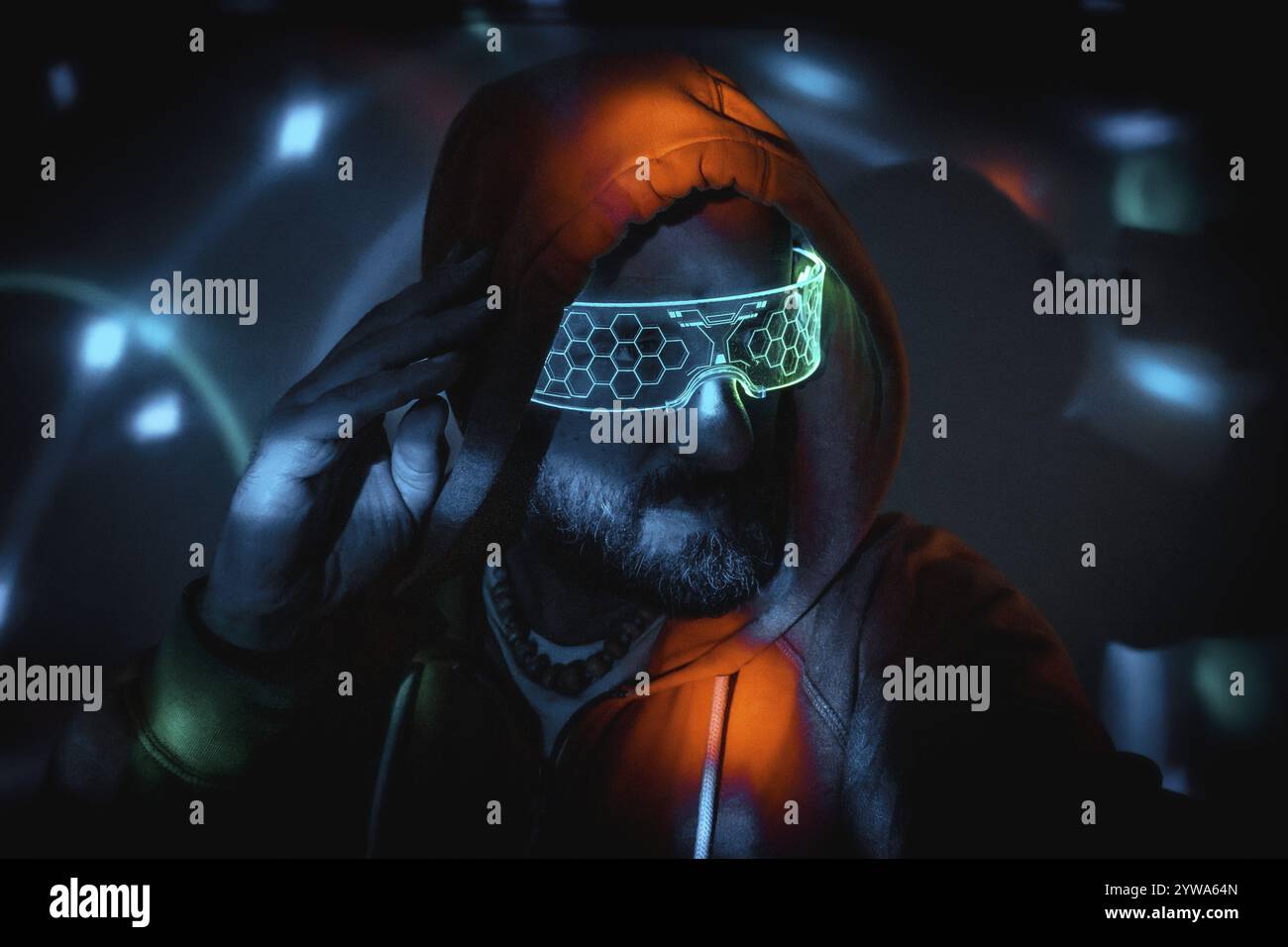 Bärtiger Mann mit futuristischer Neonbrille und Hoodie, berührte seinen Kopf und tauchte in eine Cyberpunk-Umgebung mit hellen Lichtern ein Stockfoto