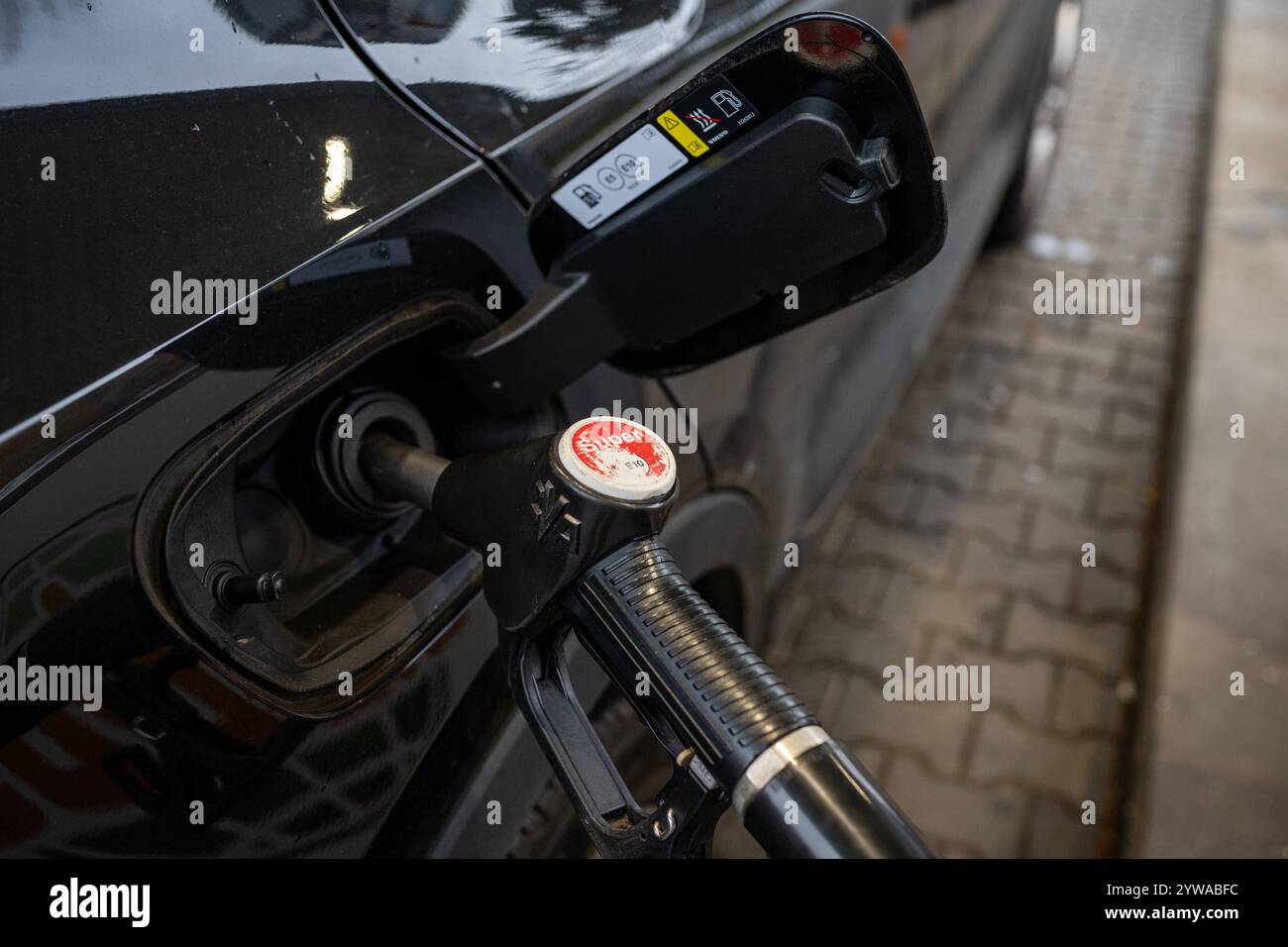 Tankvorgang an einer Tankstelle 09.12.24, Selters: Symbolfoto, Illustrationsbild, Symbolbild, Illustrationsfoto, Alltagsszene Tankvorgang an einer Tankstelle Nahaufnahme eines schwarzen Autos während eines Tankvorgangs. Die Zapfpistole ist in den Tankstutzen eingesteckt, und der Aufdruck Super E10 ist auf der Zapfpistole deutlich sichtbar. Der Hintergrund zeigt verschwommen die gepflasterte Fläche der Tankstelle. Die Szene vermittelt den alltäglichen Prozess des Betankens eines Fahrzeugs. Selters Hessen Deutschland *** Betankung an einer Tankstelle 09 12 24, Selters Symbol Foto, Abbildung Stockfoto