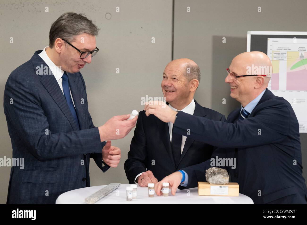 Freiberg, Deutschland. Dezember 2024. Bundeskanzler Olaf Scholz (SPD, M) und Aleksandar Vucic (l), Präsident Serbiens, stehen zusammen mit Marko Uhlig (r), Geschäftsführer von Zinnwald Lithium, bei einer kurzen Klassifizierung der Gesteinsproben im Stadt- und Bergbaumuseum. Thema des Treffens im Erzgebirge ist die nachhaltige Lithiumgewinnung für Batterien für Elektroautos. Quelle: Sebastian Kahnert/dpa/Alamy Live News Stockfoto