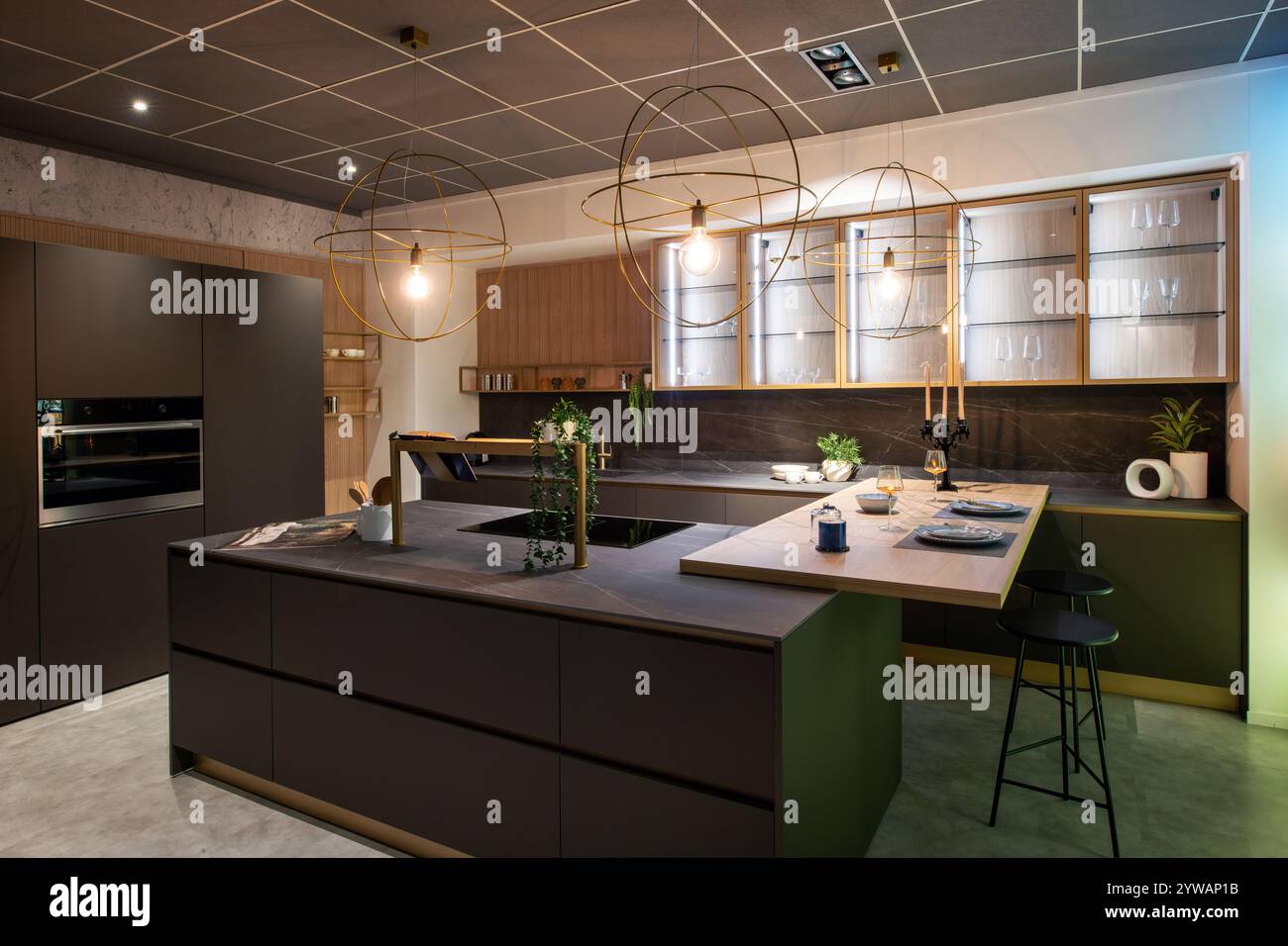 Moderne Küche mit braunen Schränken, einer Insel mit Sitzgelegenheiten und stilvollen goldenen Leuchten schaffen einen eleganten und funktionellen Raum Stockfoto