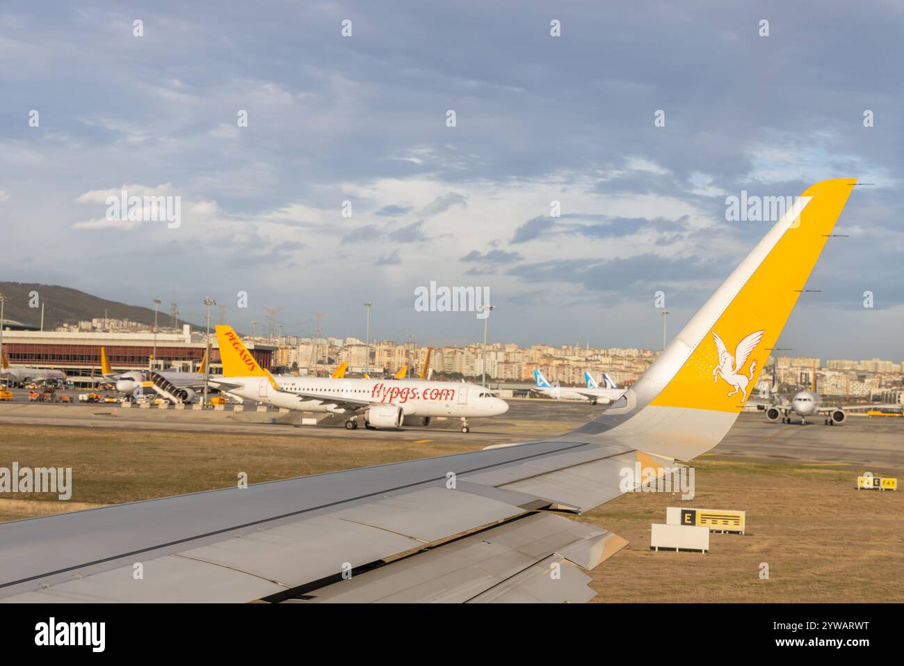 Ein Flugzeugflügel, der während der Landung oder des Starts an einem bewölkten Tag fotografiert wurde und das bewölkte Wetter und die nasse Pistenumgebung zeigt. Stockfoto
