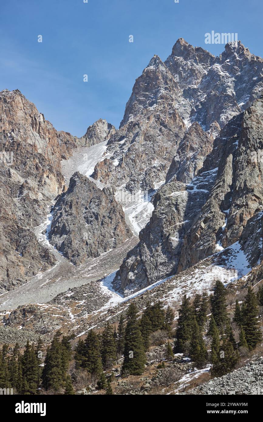 Frühlingslandschaft eingebettet in ein majestätisches Bergtal. Die hoch aufragenden Gipfel, in Schnee gehüllt. Schneebesen bedecken die Hänge, immergrüne Bäume, Stockfoto