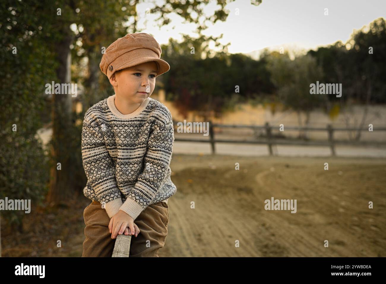 Junge in einem alten Hut und Pullover auf dem Zaun einer Reitarena Stockfoto