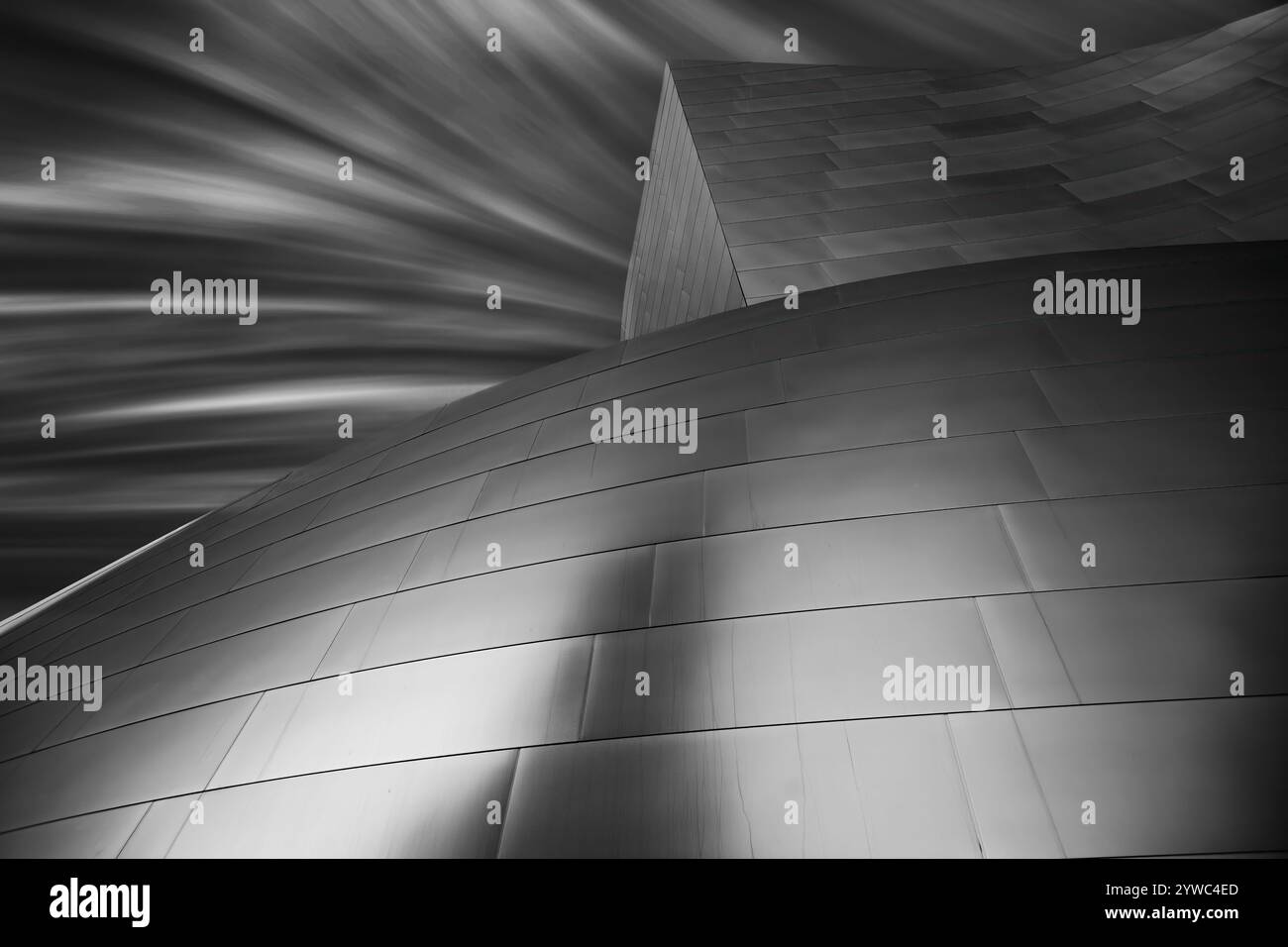 Geschwungene, glatte Metallfassungen unter einem sich schnell bewegenden bewölkten Himmel für dynamische Effekte. Stockfoto