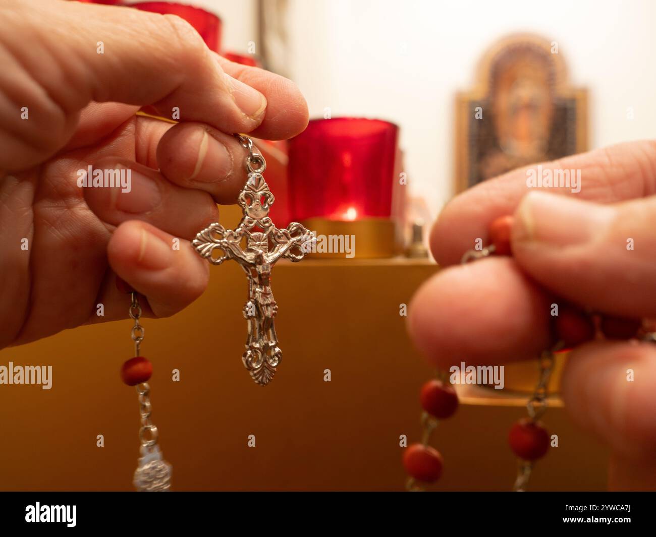 Nahaufnahme eines Rosenkranzkreuzes in der linken Hand einer kaukasischen älteren Frau mit den roten Perlen des restlichen Rosenkranzes in der rechten Hand. Photog Stockfoto