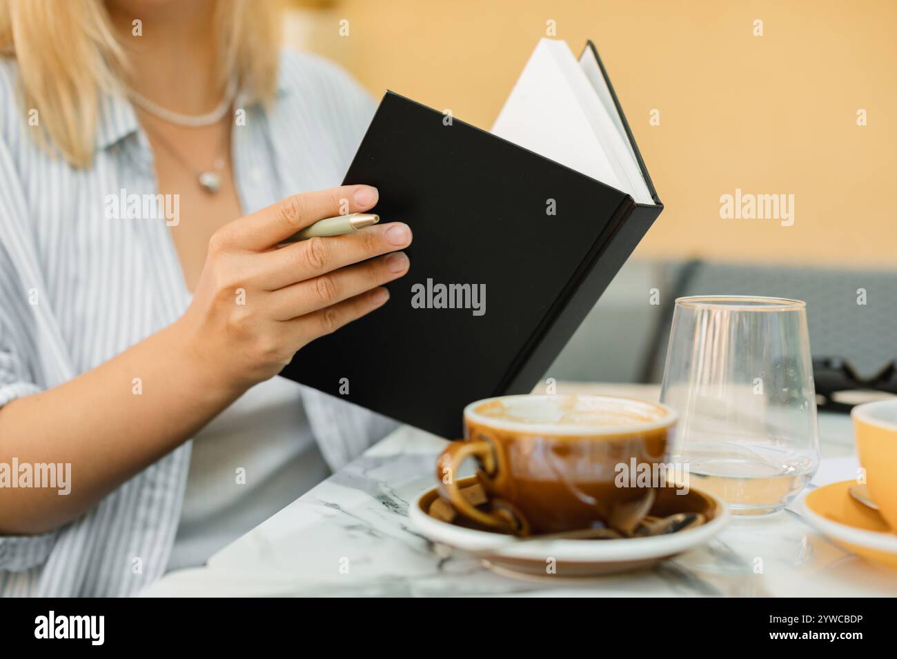 Nahaufnahme einer Frau, die in einem Café im Freien sitzt, in ein Notizbuch schreibt und Kaffee trinkt Stockfoto