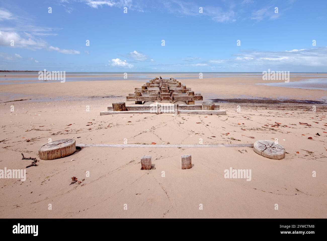 Stillgelegter Holzpier am einsamen Sandstrand bei Ebbe, der sich zum Horizont und zum blauen Himmel erstreckt, führt Burrum in Queensland Australien Stockfoto