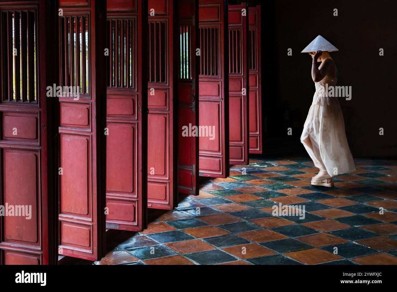 Die Einheimische Frau in weiß geht mit roten Holztüren im Minh-Mang-Grab in Hue, Vietnam Stockfoto