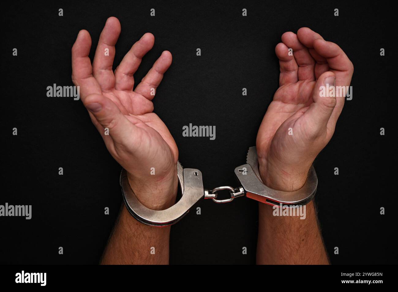 Mann mit Handschellen, der seine Handgelenke auf dunklem Hintergrund zeigt. Stockfoto