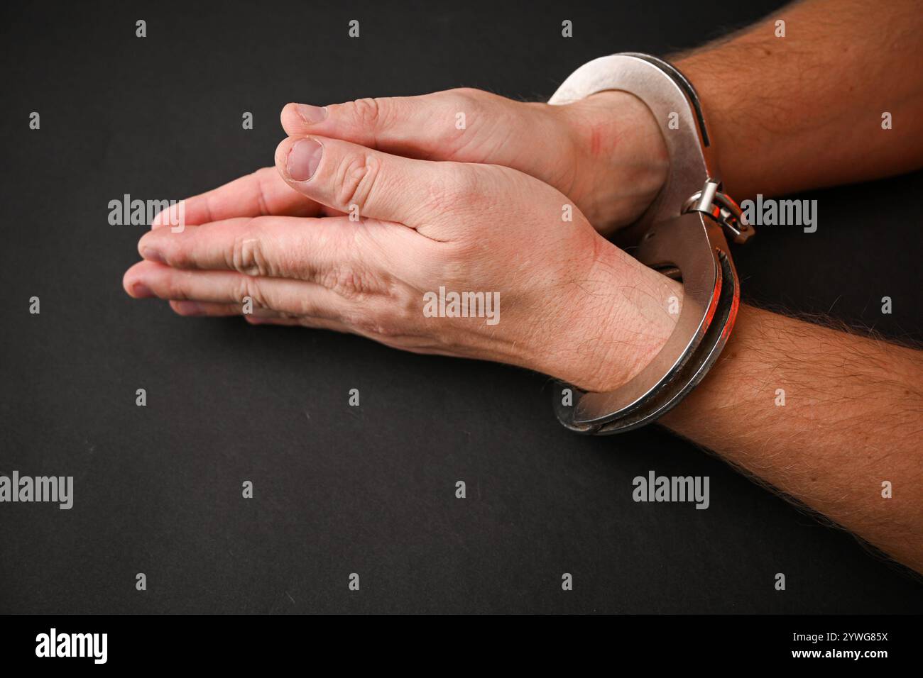 Mann mit Handschellen, der seine Handgelenke auf dunklem Hintergrund zeigt. Stockfoto