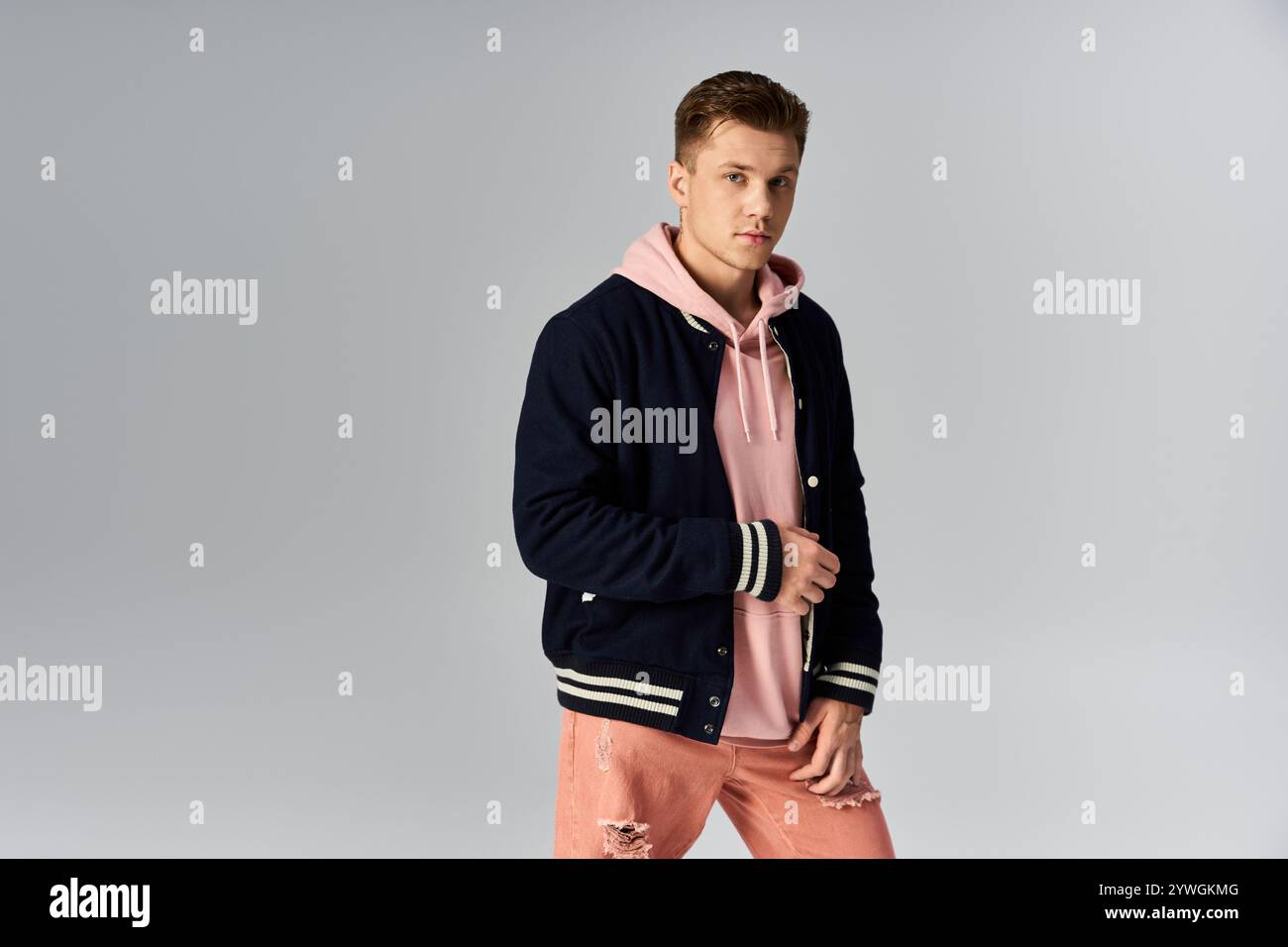 Ein junger Mann posiert stilvoll in einem legeren Outfit vor einem schlichten Hintergrund. Stockfoto