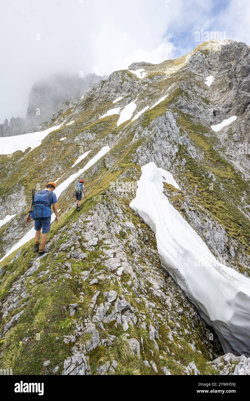 Zwei Bergsteiger mit Helmen auf einem schmalen Wanderweg, Aufstieg zur Ackerlspitze, Wolken ziehen um die Berge, Wilder Kaiser, Kaiserberg Stockfoto