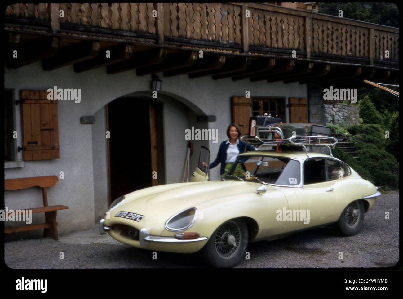 1965 Jaguar E-Type Serie I Fixed Head Coupé KTB 297C in prickelgelb mit Volldachträger und Frau an der Fahrertür auf Tour durch Europa im Juli 1968 Foto: Henshaw Archive Stockfoto