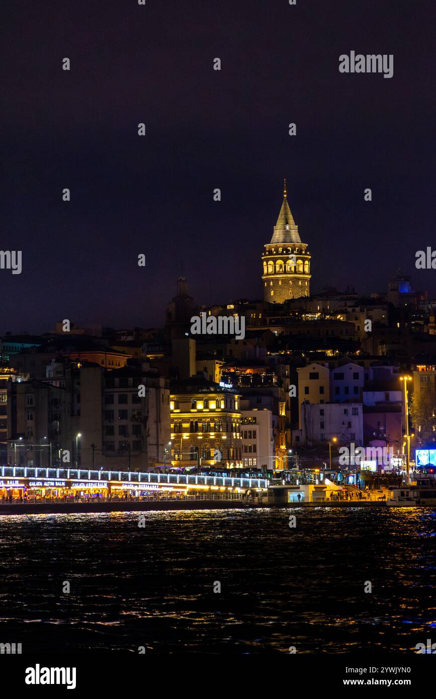 Ein atemberaubender nächtlicher Blick auf Istanbul mit dem berühmten Galata-Turm, der vor dem dunklen Himmel beleuchtet wird, mit der lebendigen Galata-Brücke. Stockfoto