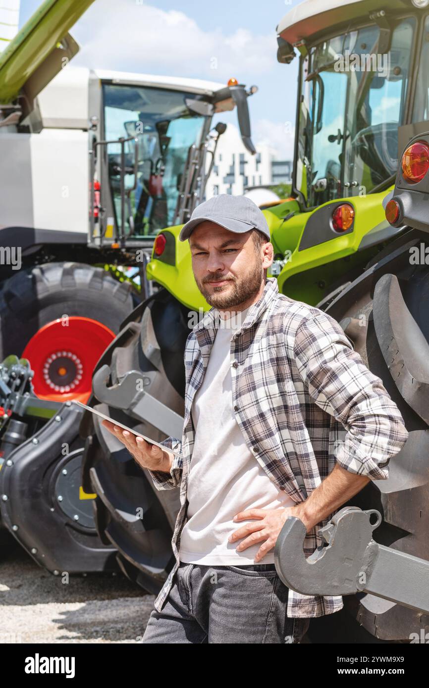 Landarbeiter mit digitalem Tablet gegen Traktor im Landmaschinenbetrieb. Stockfoto