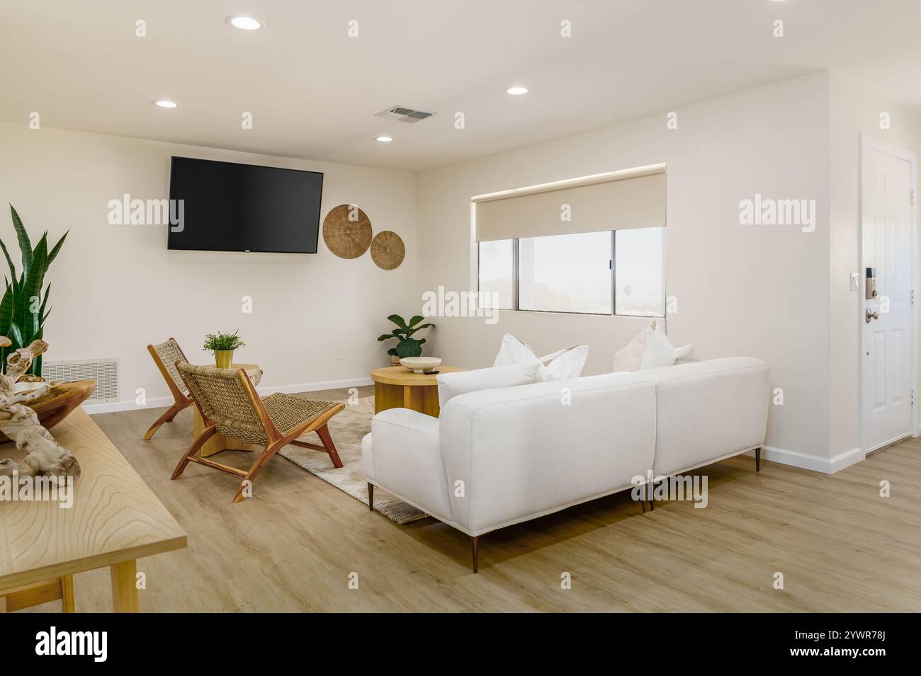Modernes Wohnzimmer mit neutralen Farben, weißem Schlafsofa, hellem Holzfußboden, zwei gewebten Stühlen und Flachbildfernseher. Stockfoto
